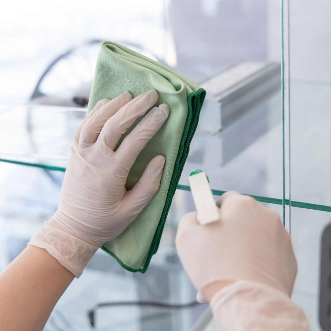 A professional cleaner in uniform carefully washing a high-rise window with a squeegee and cleaning solution.